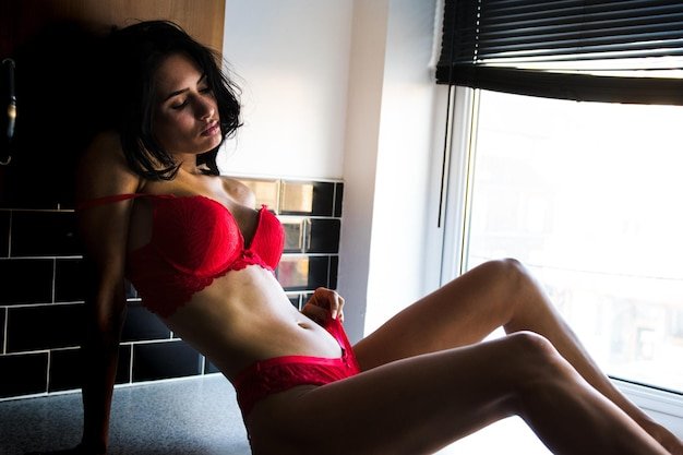 modelo-jovem-sensual-sentado-em-lingerie-vermelha-contra-a-janela_1048944-15876604